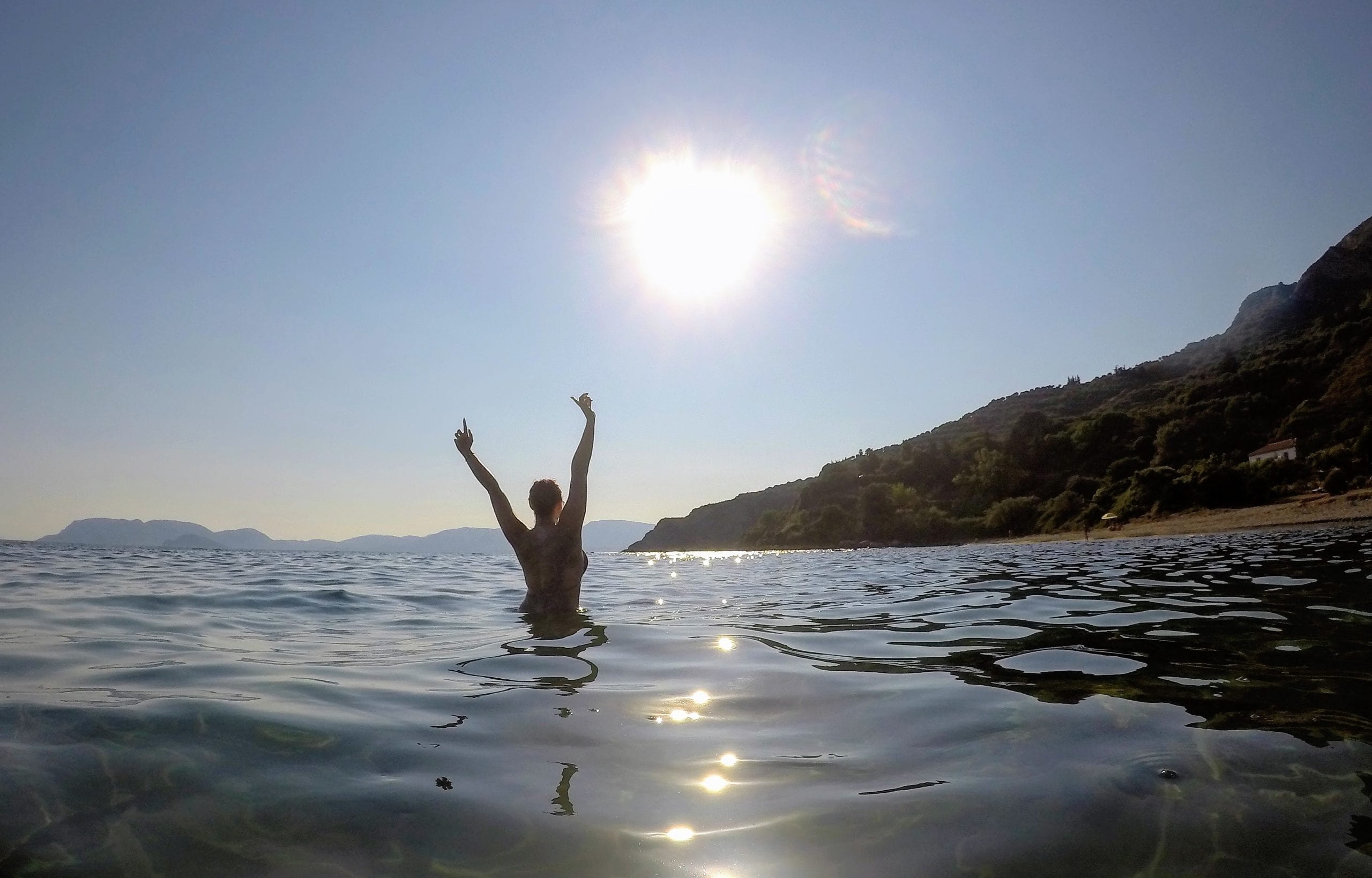 Travel to Zante | Sun Setting over the mountains as raise my arms in my bikini in the middle of the sea