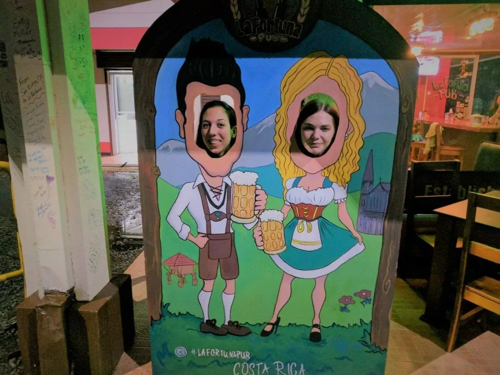 Things to do in Arenal - two women with their heads through a picture making it look like they are in traditional german outfits drinking steins