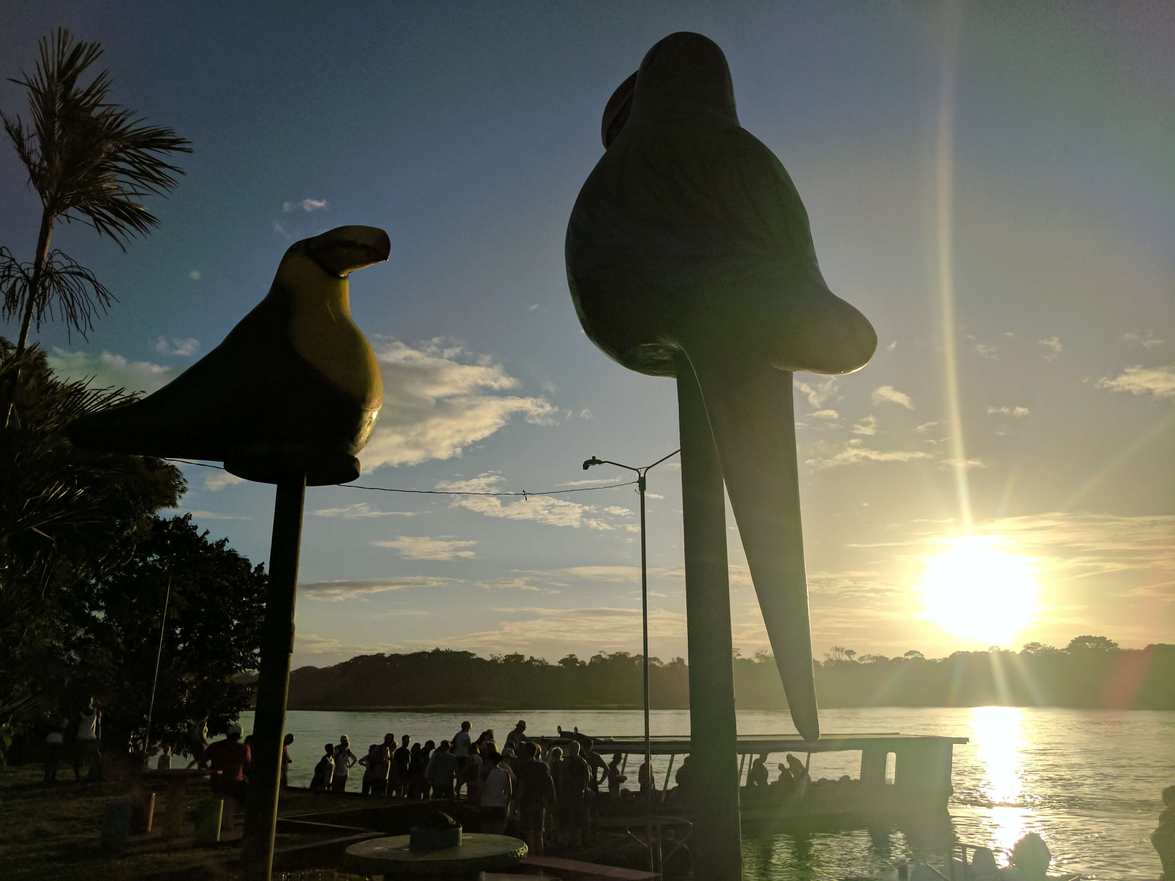 Costa Rica Itinerary - the sun setting on Tortugero village through the large statutes of tropical birds