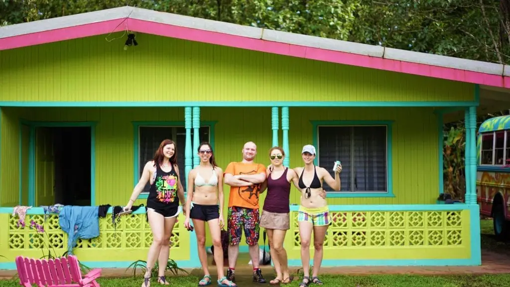 Pros and Cons of Group Tours - group of travellers looking happy outside a lime green and turquoise cabin   