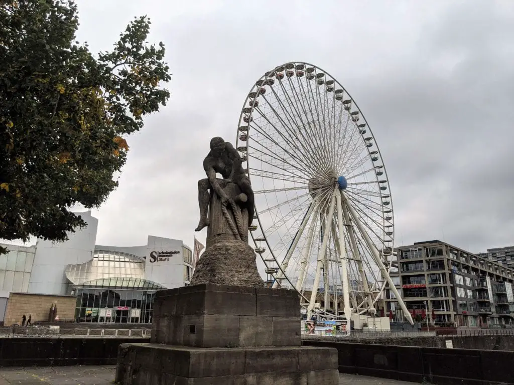 Things to do in Cologne Old Town - outside the Lindt Chocolate Factory with a view of the big wheel and a statue in the backgroun